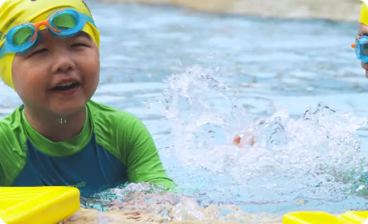 Child wearing swimming cap and goggles, learning how to swim in the shallow pool at the ActiveSg public swimming complex